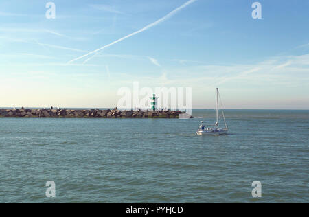 Blick vom Pier in Scheveningen Strand auf einem anderen Pier mit Leuchtturm und mann Segeln auf seinem Boot Stockfoto