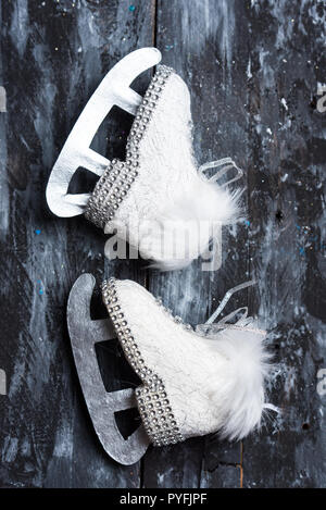 Weiß und Schwarz, Winter und Weihnachten Hintergrund, niedliche weiße Schlittschuhe auf einem schwarzen rustikalen Holztisch Stockfoto