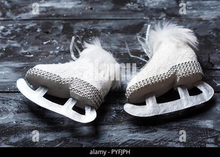 Weiß und Schwarz, Winter und Weihnachten Hintergrund, niedliche weiße Schlittschuhe auf einem schwarzen rustikalen Holztisch Stockfoto