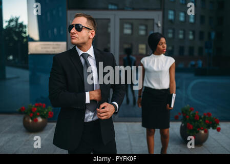 Leibwächter in Anzug und Sonnenbrille, weiblich VIP-Kunde für den Hintergrund. Security Guard ist eine riskante Beruf, professionelle Bewachung, business Personen Protein Stockfoto