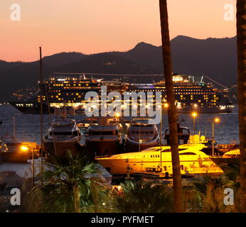 AJAXNETPHOTO. 2018. CANNES, Frankreich. - COTE D'AZUR RESORT - BLICK NACH WESTEN ÜBER DIE BUCHT VON CANNES in der Dämmerung mit Super Yachten und Kreuzfahrtschiffe im Hafen PIERRE CANTO MARINA im Vordergrund, das Kreuzfahrtschiff AIDA STELLA IN DER BUCHT vor Anker. Foto: Jonathan Eastland/AJAX REF: GX8 182509 676 Stockfoto