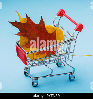 Trolley mit Blättern auf blauem Hintergrund. Konzept des Themas der Herbst Vertrieb Stockfoto