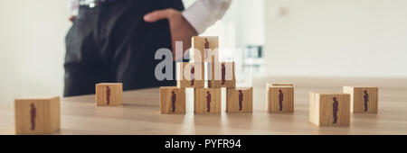 Retro Vintage Bild der Geschäftsmann stand neben einem Büro Schreibtisch mit Holzwürfeln mit Menschen Symbole in einer Pyramide. Stockfoto