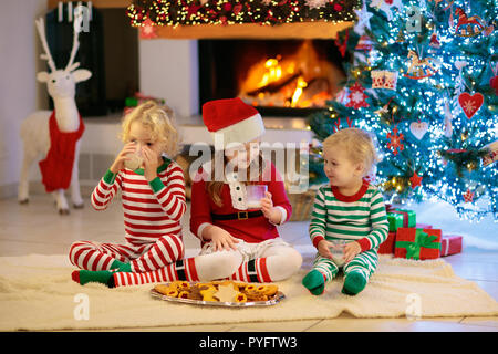 Kinder am Weihnachtsbaum und Kamin heiße Schokolade trinken und essen Cookies auf Heiligabend. Familie mit Kindern Weihnachten zu Hause feiern. Junge und Mädchen Stockfoto