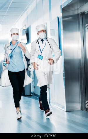 Männliche und weibliche Ärzte mit digitalen Tablet und Zwischenablage im Krankenhaus Flur laufen Stockfoto