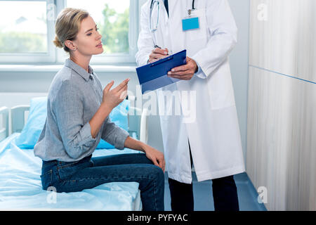Zugeschnittenes Bild der männlichen Arzt mit Zwischenablage für weibliche Patienten im Krankenhaus Zimmer Stockfoto