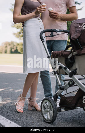 Zugeschnittenes Bild der Eltern halten Eis und in der Nähe von Kinderwagen in Park Stockfoto