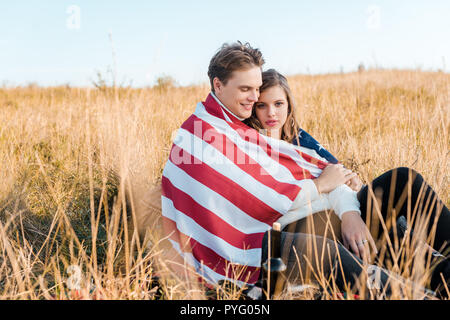 Lächelndes Paar mit amerikanischen Flagge auf ländlichen Wiese, Tag der Unabhängigkeit Konzept Stockfoto