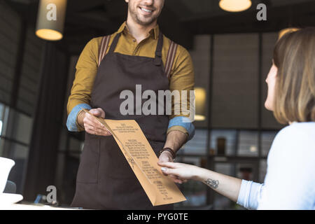 7/8 Schuß von lächelnden Kellner zeigen Menü Liste der weiblichen Kunden im Cafe Stockfoto