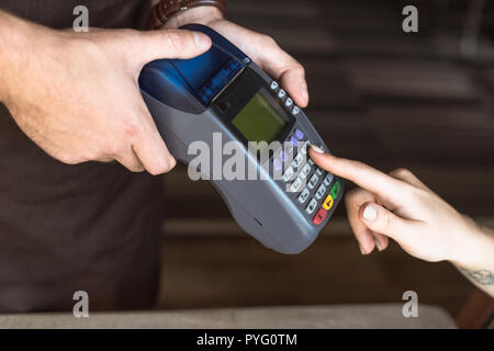 7/8 Schuß von Kellner holding Payment Terminal während der Kunde Eingabe der Pin im Cafe Stockfoto