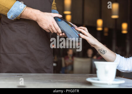 7/8 Schuß von Kellner holding Payment Terminal während der Eingabe der Pin im Cafe Stockfoto