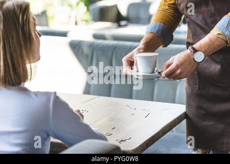 7/8 Schuß von Kellner servieren Tasse Cappuccino für weibliche Kunden im Cafe Stockfoto