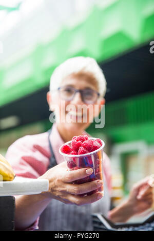 Portrait der älteren Frau verkauft Himbeeren auf dem Markt Stockfoto