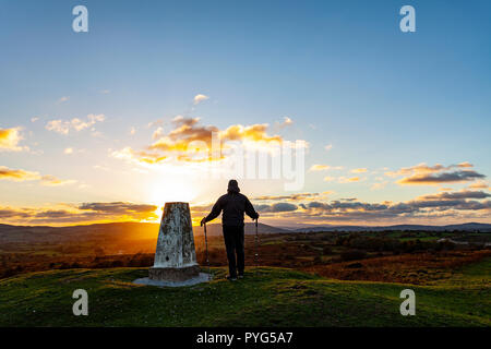 Flintshire, Nord Wales am 27. Oktober 2018. UK Wetter: Ein arctic Blast salzen Schnee und eisigen Temperaturen für viele Teile des Vereinigten Königreichs. Einen spektakulären Sonnenuntergang über dem Clwydian Hügel reichen von oben Halkyn Berg auf dem Flintshire Seite der Palette als Hügel Walker nimmt in den Sonnenuntergang gegen Herunterfallen sichern die Trigonometrie Punkt © DGDImages/AlamyNews Stockfoto