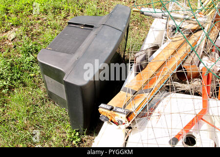 Alte Fernseher gedumpten und Links im Garten zusammen mit anderen sperrigen Müll. Alter FERNSEHER weggeworfen neben einer Wand mit einem Stapel von gemischten Müll in der Natur. Stockfoto