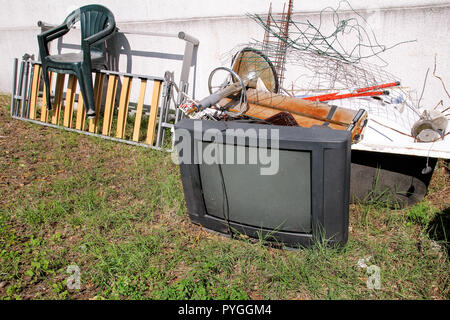 Alte Fernseher und den Rest von sperrigen Müll. Alter FERNSEHER weggeworfen neben einer Wand mit einem Stapel von gemischten Müll. in natürlicher Umgebung. Recycling Industrie. Stockfoto