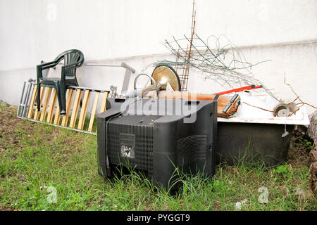 Alte Fernseher und den Rest von sperrigen Müll. Alter FERNSEHER weggeworfen neben einer Wand mit einem Stapel von gemischten Müll. in natürlicher Umgebung. Recycling Industrie. Stockfoto
