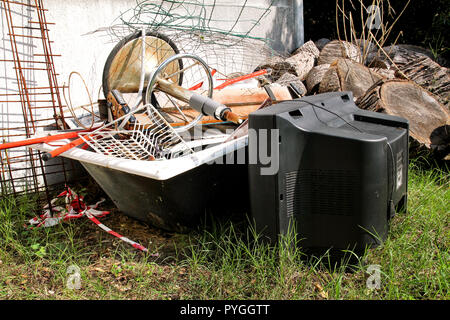Alte Fernseher und den Rest von sperrigen Müll. Alter FERNSEHER weggeworfen neben einer Wand mit einem Stapel von gemischten Müll. in natürlicher Umgebung. Recycling Industrie. Stockfoto