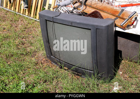 Alte Fernseher gedumpten und Links im Garten zusammen mit anderen sperrigen Müll. Alter FERNSEHER weggeworfen neben einer Wand mit einem Stapel von gemischten Müll in der Natur. Stockfoto