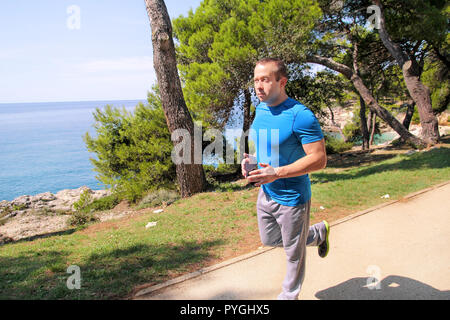 Passen junge Mann joggen auf einem laufenden Trail entlang der Küste. Freizeit fitness Athlet in Sportswear genießt körperliche Aktivitäten im Sommer. Stockfoto