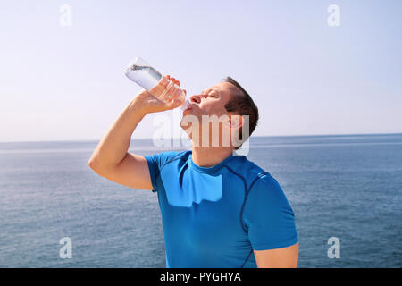 Ein Athlet eine Pause während der Ausbildung, Trinken frisches sauberes Wasser aus einer Flasche, ruht und genießt die saubere Luft, mit einem schönen blauen Himmel. Stockfoto