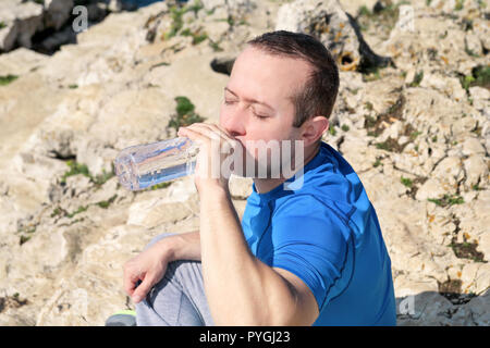 Ein Athlet eine Pause während der Ausbildung, Trinken frisches sauberes Wasser aus einer Flasche, ruht und genießt die saubere Luft, mit einem schönen blauen Himmel. Stockfoto