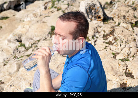 Ein Athlet eine Pause während der Ausbildung, Trinken frisches sauberes Wasser aus einer Flasche, ruht und genießt die saubere Luft, mit einem schönen blauen Himmel. Stockfoto