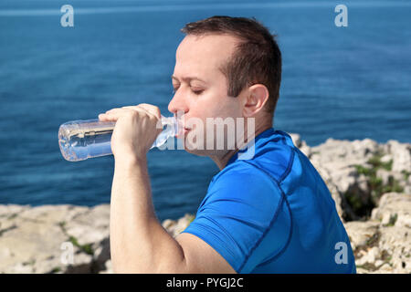 Ein Athlet eine Pause während der Ausbildung, Trinken frisches sauberes Wasser aus einer Flasche, ruht und genießt die saubere Luft, mit einem schönen blauen Himmel. Stockfoto
