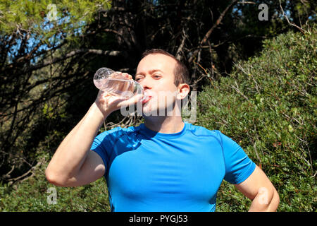 Ein Athlet eine Pause während der Ausbildung, Trinken frisches sauberes Wasser aus einer Flasche, ruht und genießt die saubere Luft, mit einer schönen Landschaft Natur Stockfoto