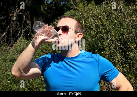 Ein Athlet eine Pause während der Ausbildung, Trinken frisches sauberes Wasser aus einer Flasche, ruht und genießt die saubere Luft, mit einer schönen Landschaft Natur Stockfoto