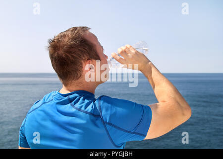 Ein Athlet eine Pause während der Ausbildung, Trinken frisches sauberes Wasser aus einer Flasche, ruht und genießt die saubere Luft, mit einem schönen blauen Himmel. Stockfoto