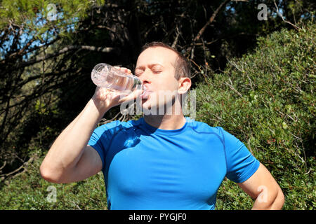 Ein Athlet eine Pause während der Ausbildung, Trinken frisches sauberes Wasser aus einer Flasche, ruht und genießt die saubere Luft, mit einer schönen Landschaft Natur Stockfoto