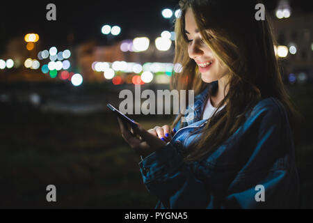Blogger Hipster mit in den Händen gadget Handy. Frau zeigt mit dem Finger auf Blank Screen Smartphone auf Hintergrund bokeh Licht in der Nacht atmosphärischen ci Stockfoto