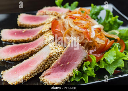 Close Up Still Life von gebratenem Thunfisch Steaks verkrustet mit Kräutern und Sesam auf Dunkelgrau Oberfläche Stockfoto
