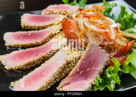 Close Up Still Life von gebratenem Thunfisch Steaks verkrustet mit Kräutern und Sesam auf Dunkelgrau Oberfläche Stockfoto