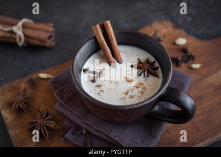 Traditionelle indische Masala Chai Tee in Keramik Tasse mit Zutaten. Würziger schwarzer Tee mit Milch auf rustikalen dunklen Hintergrund, aus der Nähe. Stockfoto