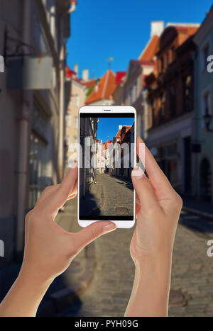 Ein Tourist ist ein Foto von der Straße der alten Stadt an einem sonnigen Tag in Tallinn, Estland, und auf einem Mobiltelefon Stockfoto