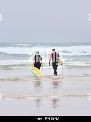 Ein Mann und eine Frau gehen in das Meer mit Body Boards, Perranporth Beach, Cornwall, England, Großbritannien Stockfoto