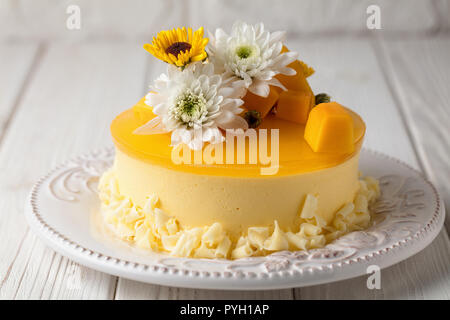 Mango Cheesecake mit gelben Gelee Topping, mit Blumen und frische Mango Stücke auf weißem Hintergrund, horizontale Zusammensetzung Stockfoto