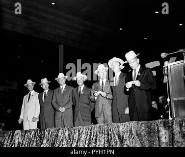 (4 Juli 1962) - - - Die ursprünglichen sieben Mercury Astronauten, jedem tragen Neue cowboyhüte und ein Abzeichen in der Form eines Sterns, abgebildet auf der Bühne an der Sam Houston Coliseum. Eine große Menschenmenge war an Hand sie zu Houston, Texas begrüßen zu dürfen. Zu recht sind Astronauten M. Scott Carpenter, L. Gordon Cooper jr., John Glenn Jr., Virgil Grissom, Walter I. M. Schirra jr., Alan B. Shepard, Jr., und Donald K. Slayton verlassen. Senator John Tower (R-Texas) ist ganz rechts im Hintergrund zu sehen. Stockfoto