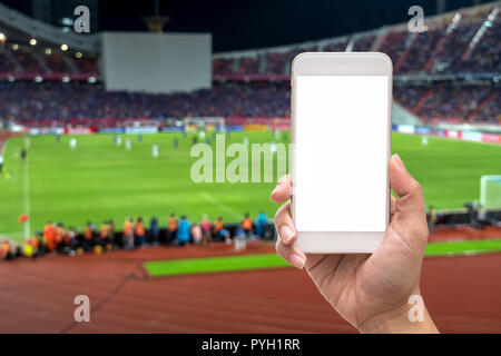 Weibliche Hand, die eine Mobile Smartphone Touchscreen auf der Fotograf, Foto bei Player in abstrakten verwischt verschwommenes Foto von Fußball-stadi Stockfoto