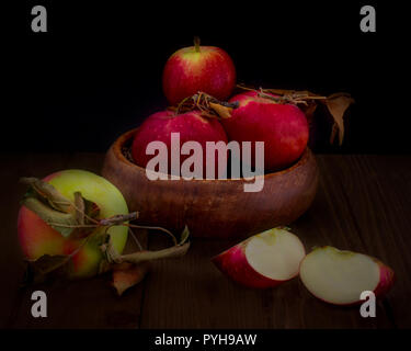 Schale mit ausgesuchten Äpfel auf schwarzem Hintergrund mit einem vollständigen und einem Schnitt von Apple auf Holztisch - Herbst Zusammensetzung Stockfoto