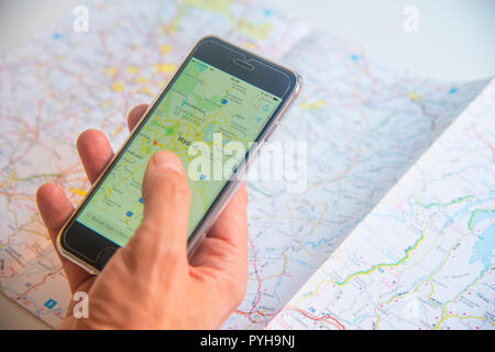 Mann hält ein Smartphone mit einer Karte und road map als Hintergrund. Stockfoto