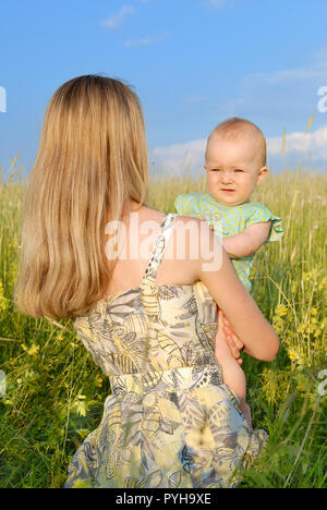 Junge Frau mit Kind auf dem Green Field, blauen Himmel im Hintergrund Stockfoto