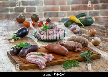 Auswahl französischer Rohwurst mit Rucola Blätter in einem Holzbrett, Gemüse auf dem Tisch auf alten roten Backsteingebäude aus dem Hintergrund. Stockfoto