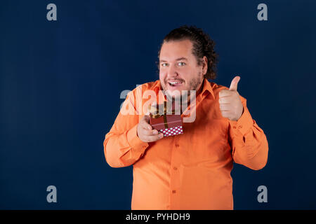 Funny fat man in orangefarbenen T-Shirt öffnet sich eine Box mit einem Geschenk Stockfoto