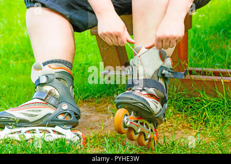 Der Skater bindet die Rollschuhe auf der Bank. Detailansicht Inline Skates in das grüne Gras. In-line Skating. Bekämpfung der Schnürsenkel auf Rollschuhen Stockfoto