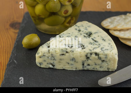 Blue Cheese Keil mit Defokussierten Glas grüne Oliven und Cracker im Hintergrund Stockfoto