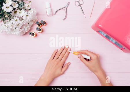 Ansicht von oben weibliche Hände pflegende Haut nach gel Maniküre in der Nähe von UV-Lampe, Werkzeuge und Strauß Blumen auf rosa Tabelle. Flach Anordnung Frau Stockfoto