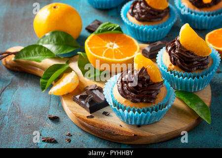 Orange Cupcakes mit Schokolade und Sahne frische Mandarinen auf einem blauen Stein oder Beton. Stockfoto
